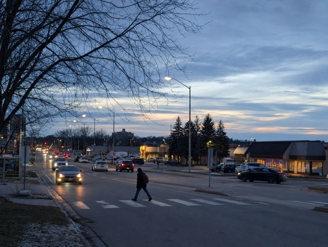 Single-storey plazas along a suburban road at dusk, with shops from every local industry side by side